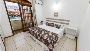 A bedroom with a bed, bedside tables, a nightstand, a window with curtains, and an air conditioning unit. - Morro das Pedras Clube Hotel (Florianópolis)