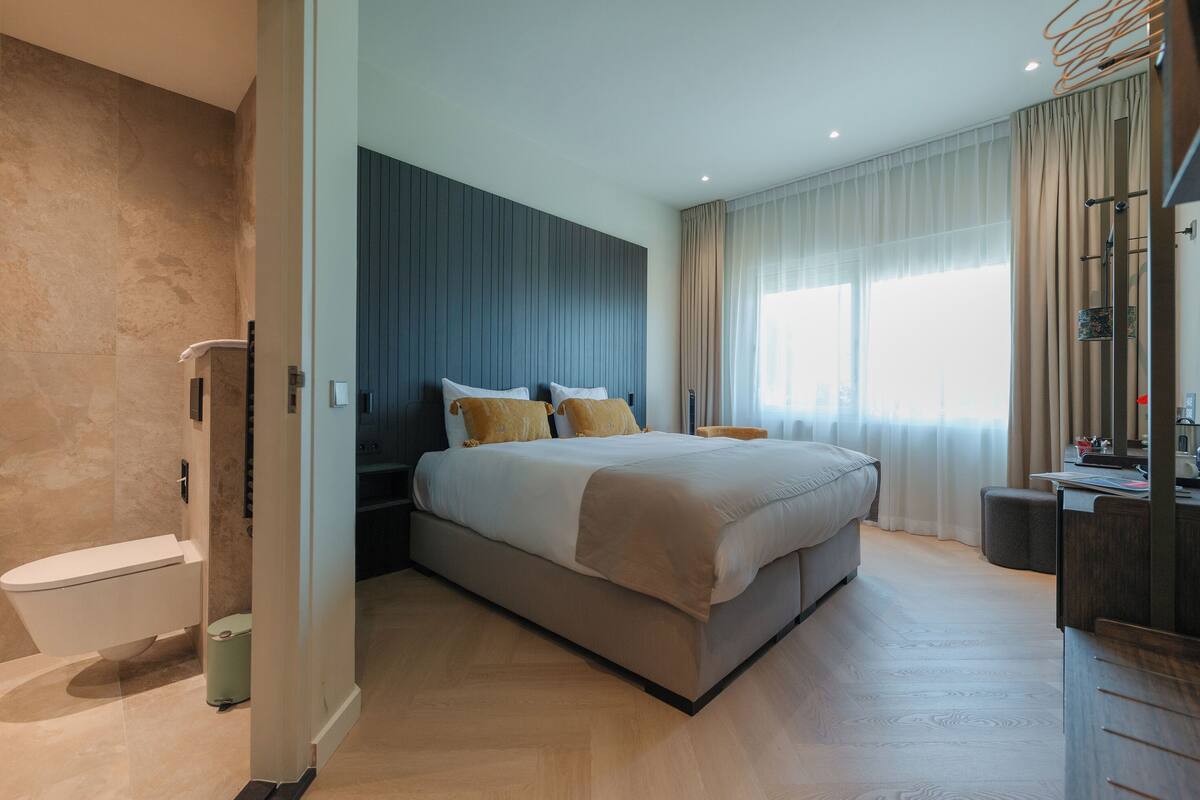 A modern bedroom with a large bed, a built-in wardrobe, and a bathroom with a toilet and shower.