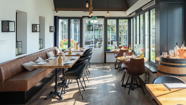 A modern restaurant with a long wooden bench, black chairs, and a bar area with a barrel.