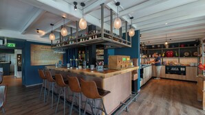 A modern bar area with a wooden counter, bar stools, and hanging pendant lights.
