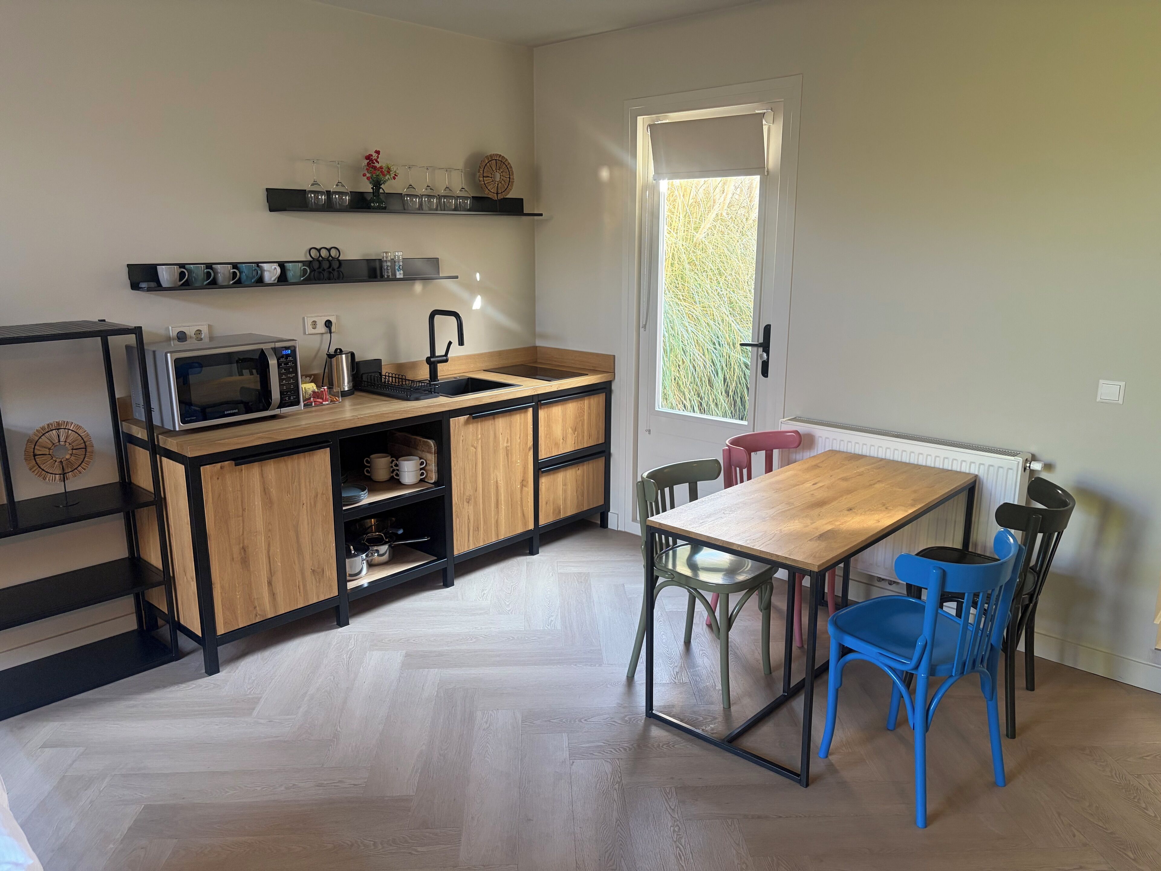 Una cocina moderna con encimera de madera, microondas integrado y un lavabo. Hay una mesa de comedor con sillas y un ventanal con vistas a árboles.