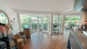 A spacious lobby with wooden flooring, a reception desk, and a large window offering a view of greenery outside.