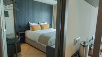 Una habitación de hotel con cama, mesita de noche, maleta y un calentador de pared.