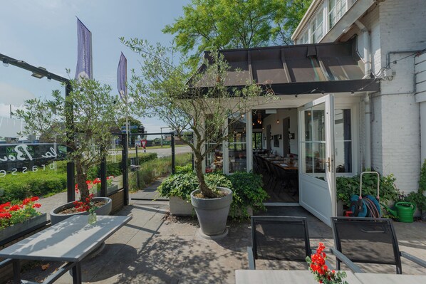 An outdoor seating area with tables and chairs, potted plants, and a covered patio. - Boutique Hotel Herbergh Amsterdam Airport (Badhoevedorp)