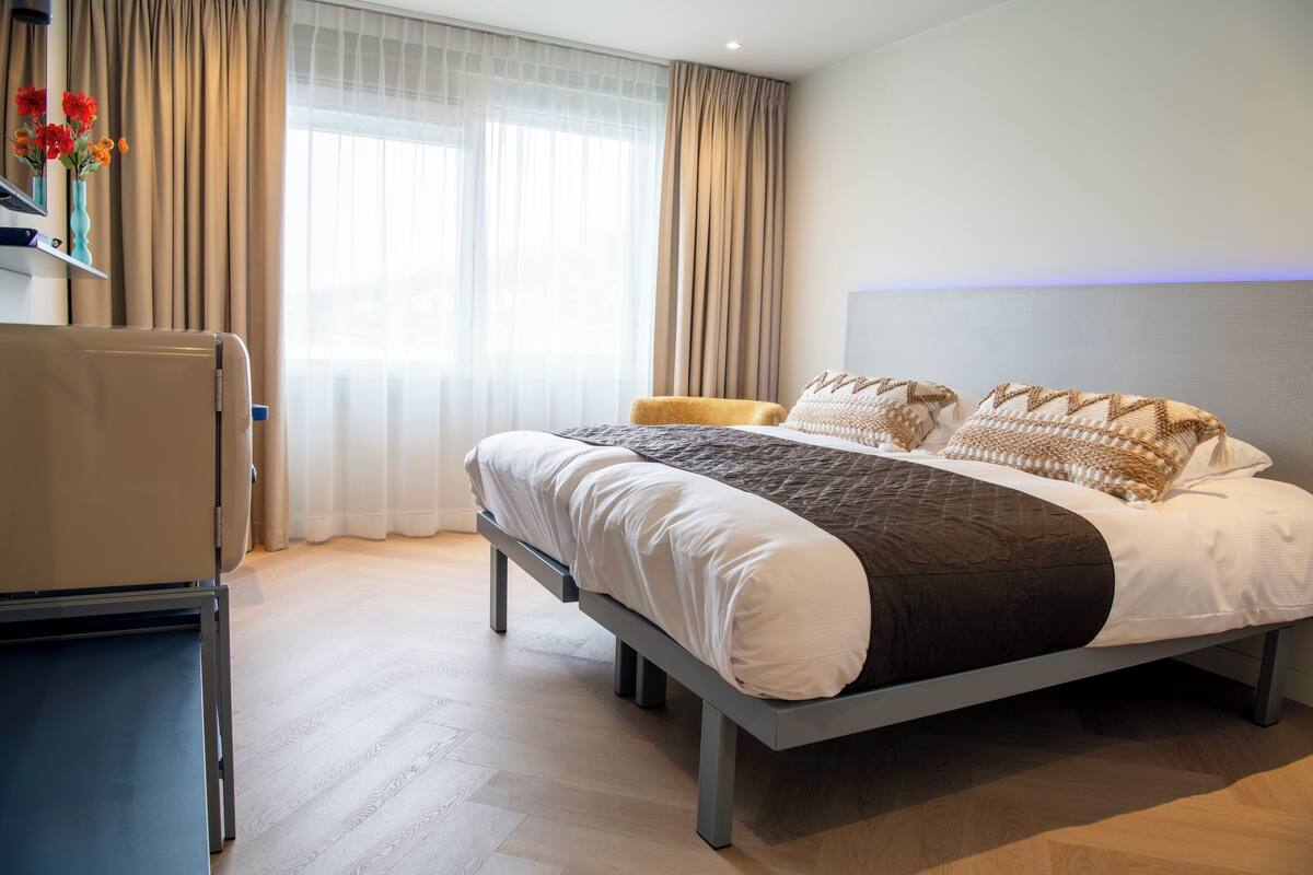 A modern hotel room with a large bed, a bedside table, and a desk with a chair.
