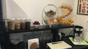 Una barra de desayuno con recipientes de cereal, cuencos de fruta y una cafetera.