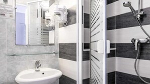 Un baño con lavamanos blanco, espejo y ducha con cabezal de ducha manual.