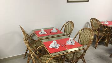 Un coin repas avec des chaises et des tables en osier, chaque table étant agrémentée de tasses et de soucoupes blanches posées sur des sets de table rouges.