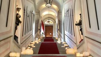 A grand staircase with red carpet, flanked by wall-mounted weapons and a chandelier.