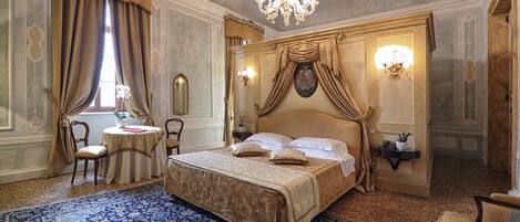 Een luxueuze slaapkamer met een groot bed, sierlijke gordijnen, een kroonluchter en een kamerbreed tapijt.