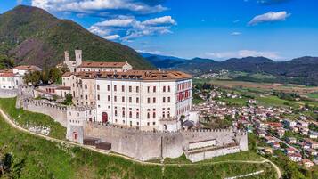 A historic building with a fortified wall, surrounded by a town and mountains.