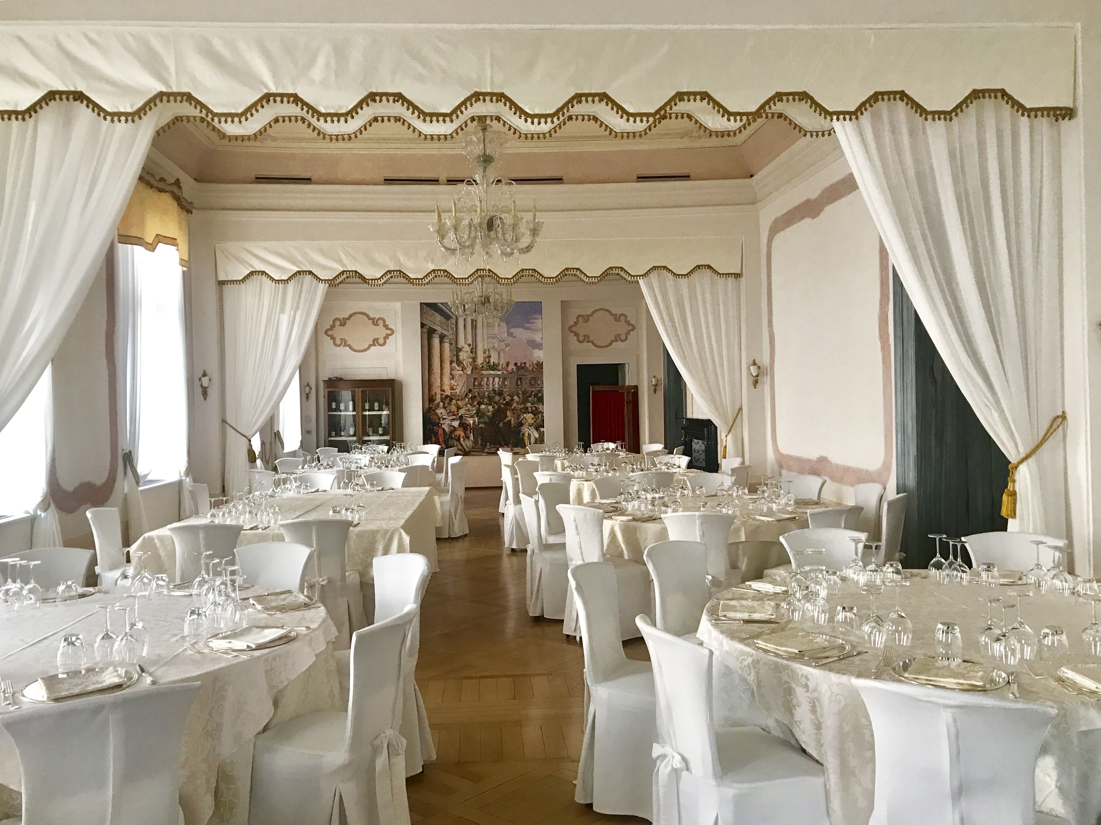 A banquet hall with round tables set for dining, white chairs, and a large chandelier.