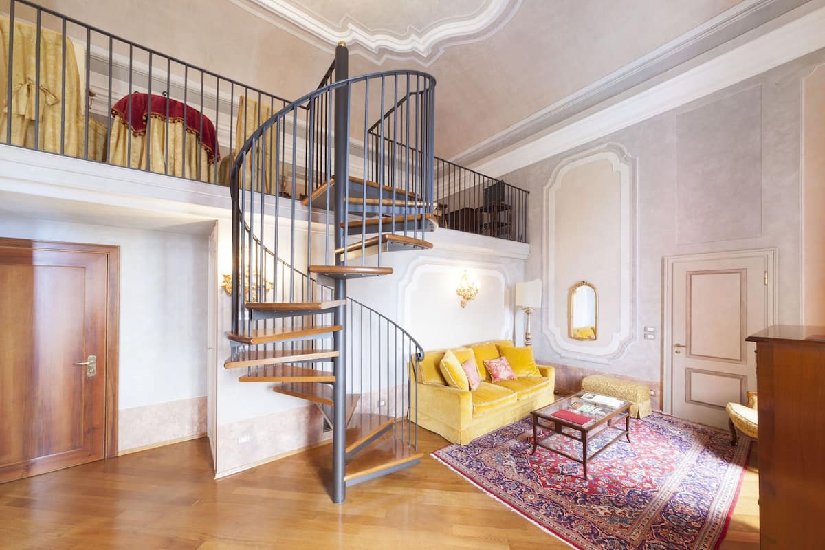 A spacious living area with a wooden staircase, a yellow sofa, a patterned rug, and a wooden cabinet.