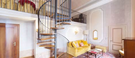 A spacious living area with a wooden staircase, a yellow sofa, a patterned rug, and a wooden cabinet.