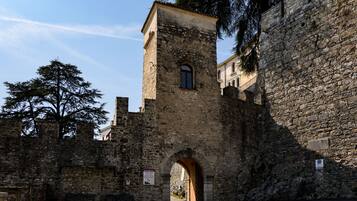 Una torre de piedra con una entrada arqueada, parte de un edificio histórico con un muro de piedra y un árbol al fondo.