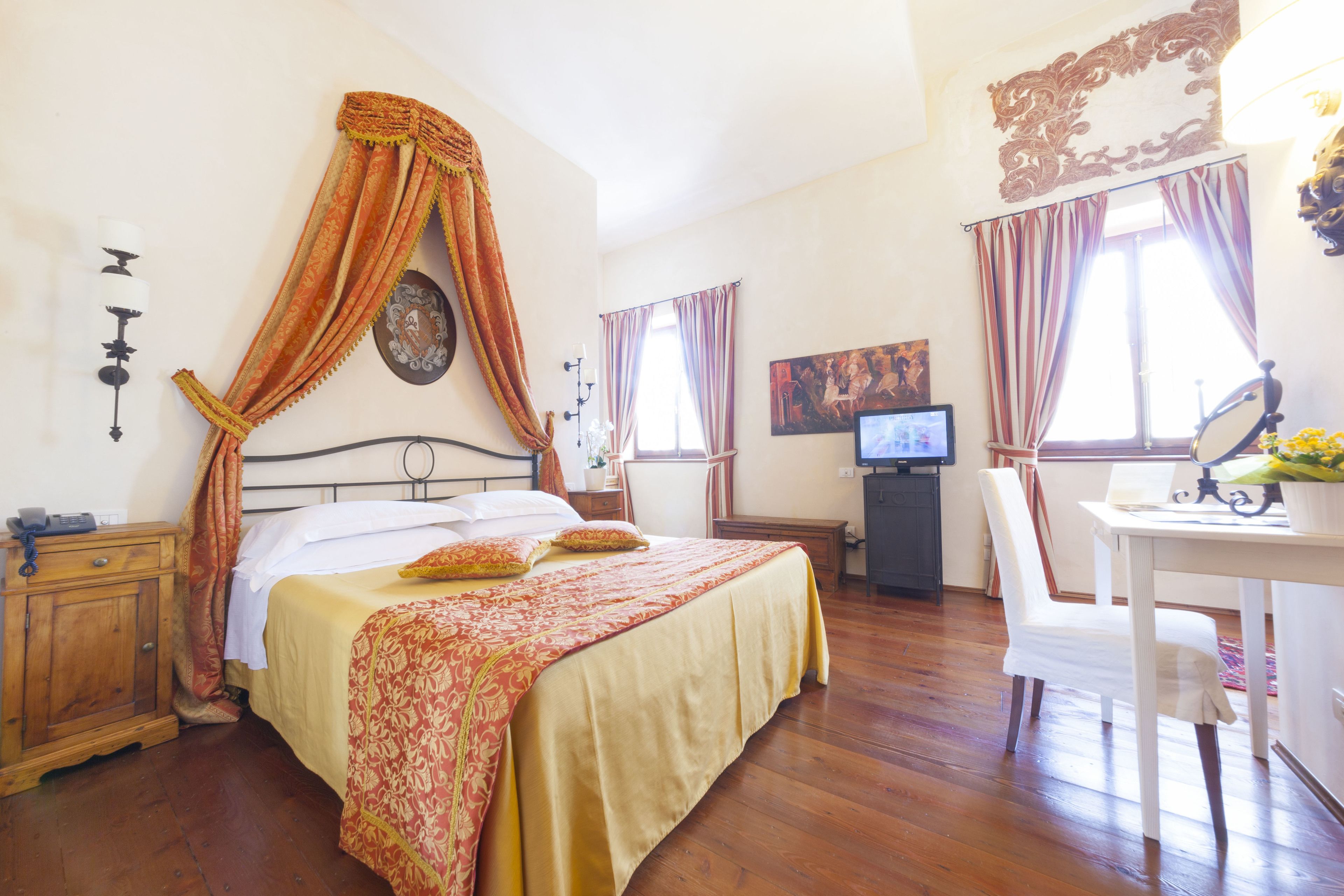 A bedroom with a four-poster bed, a desk with a chair, a television, and a small cabinet.
