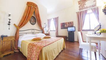 A bedroom with a four-poster bed, a desk with a chair, a television, and a small cabinet.