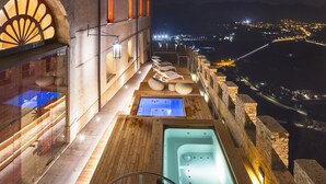 A rooftop terrace with a hot tub and lounge chairs overlooking a cityscape at night.