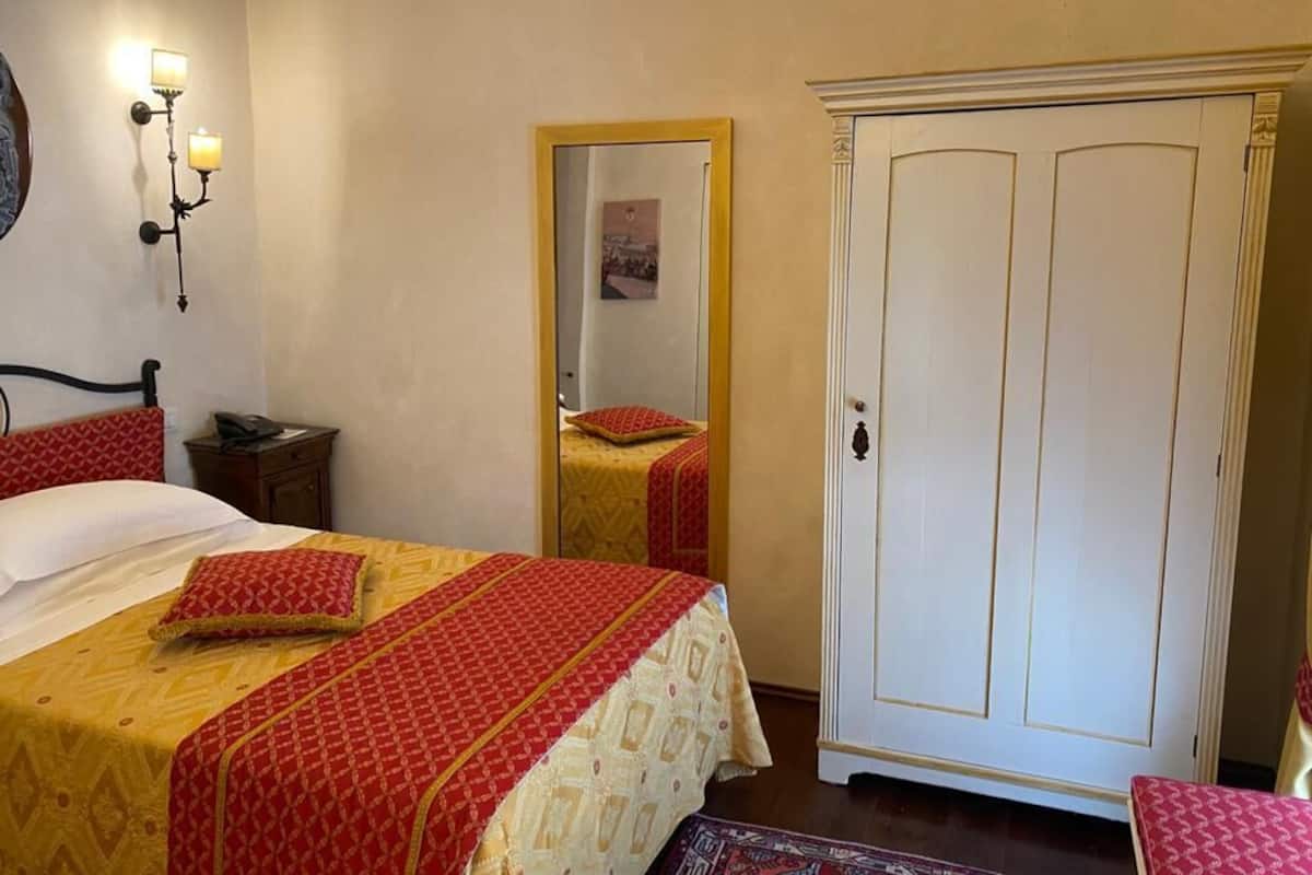 A bedroom with a bed, a wardrobe, a nightstand, and a mirror.