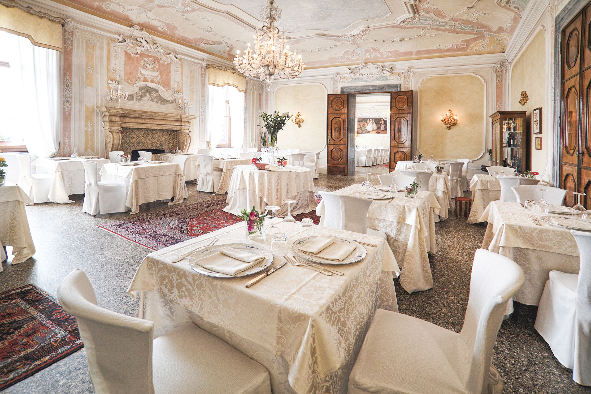 A formal dining room with multiple tables set for a meal, ornate ceiling, and classical architecture.