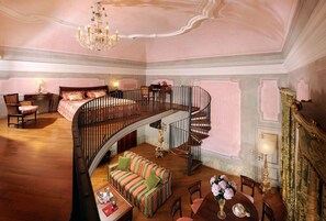 A spacious bedroom with a curved staircase, a large bed, a sitting area with a sofa, and a dining table with chairs. - Castelbrando (Cison di Valmarino)
