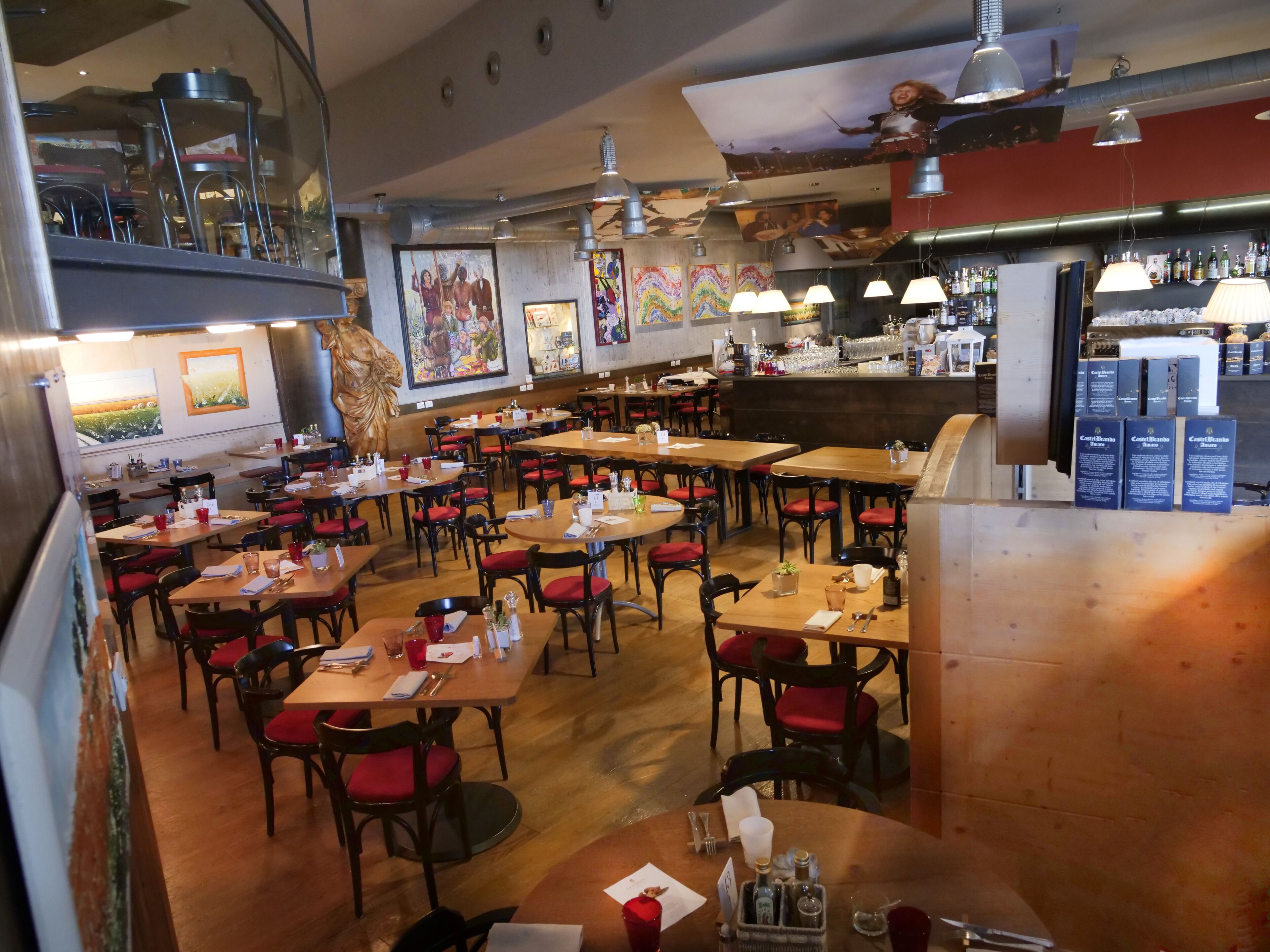 Um restaurante com várias mesas, cadeiras, uma área de bar e diversas obras de arte nas paredes.