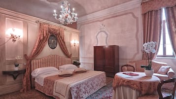 Una camera da letto con un letto grande, un lampadario, un armadio in legno, un tavolino con un vaso e una finestra con tende.