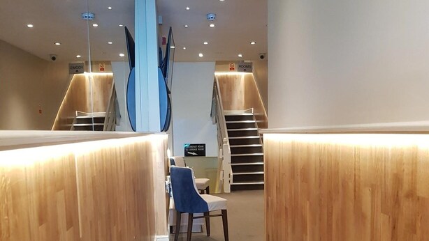 Un hall d’hôtel moderne avec des panneaux de bois, un comptoir d’accueil et un escalier menant aux étages supérieurs.