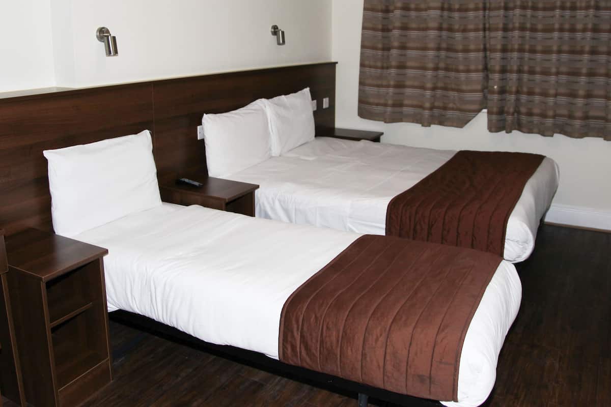 Een hotelkamer met twee eenpersoonsbedden, houten hoofdeinden, een nachtkastje, een kleine tafel en een bruin gordijn.