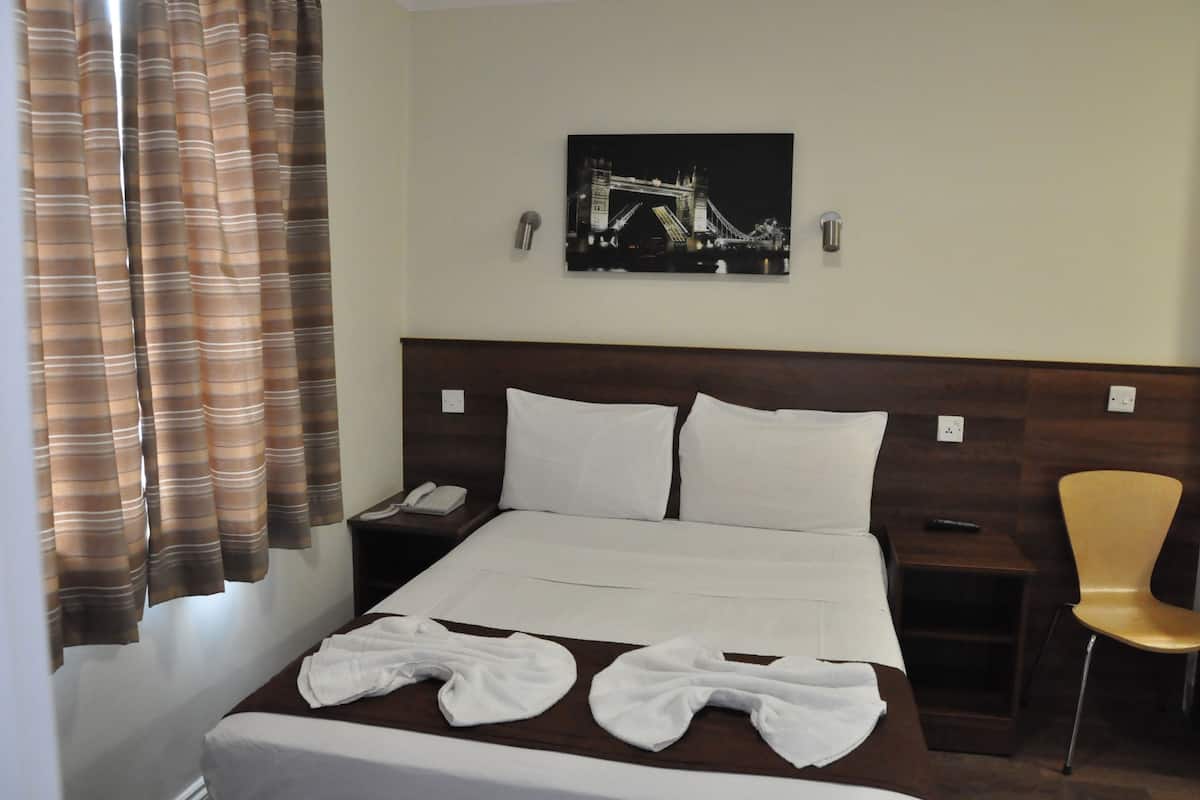 Een hotelkamer met een bed, een stoel, een schilderij van een brug en een telefoon op het nachtkastje.