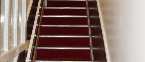 A staircase with red carpeted steps and metal railings, leading to a room with a clock and a blue wall.