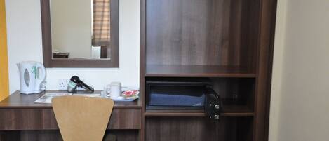 A hotel room with a wooden desk, a chair, a microwave, a coffee maker, a trash bin, and a mirror.
