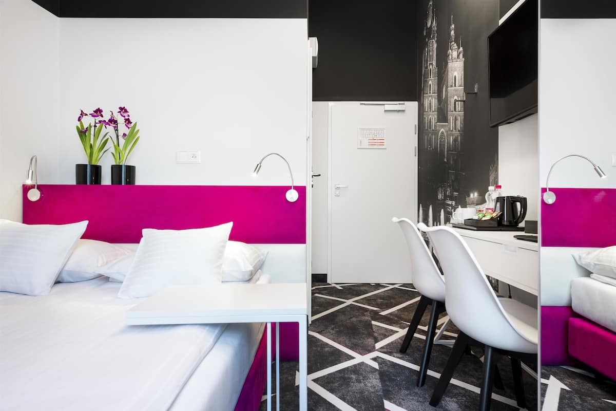Habitación de hotel con una cama, un escritorio y una silla. Se observa una puerta con un letrero.