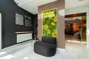 A modern lobby with a black sofa, a green wall with a 'Go Green' sign, and a reception desk. - Best Western Plus Krakow Old Town (Kraków)