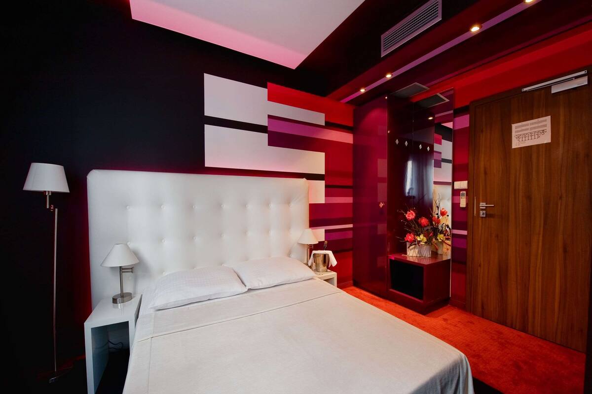 Una habitación de hotel moderna con una cama grande, una mesita de noche, un escritorio y un armario de madera.