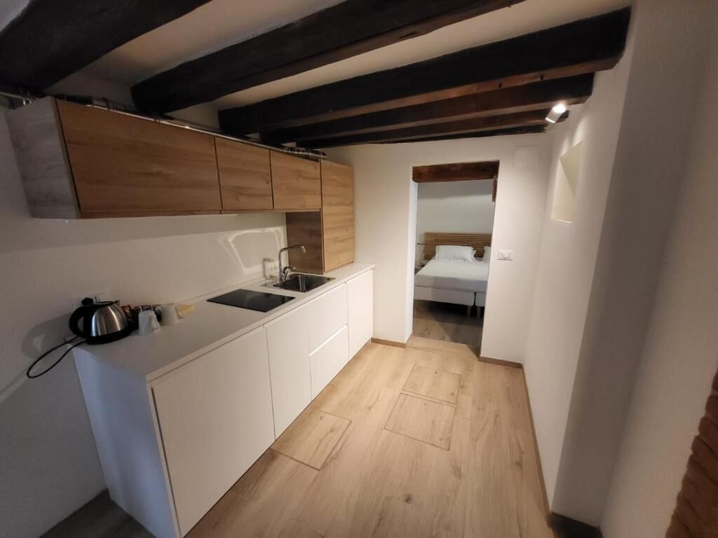 A compact kitchen with white cabinets, a sink, and a kettle. There is a wooden ceiling beam and a small window.