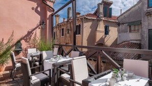 An outdoor patio with tables and chairs, overlooking a row of traditional buildings with red-tiled roofs. - Ca' Dei Conti (Venice)