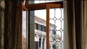 A room with a sofa set, a small table with a magazine, and a view through a window with a metal grid. - Ca' Dei Conti (Venice)