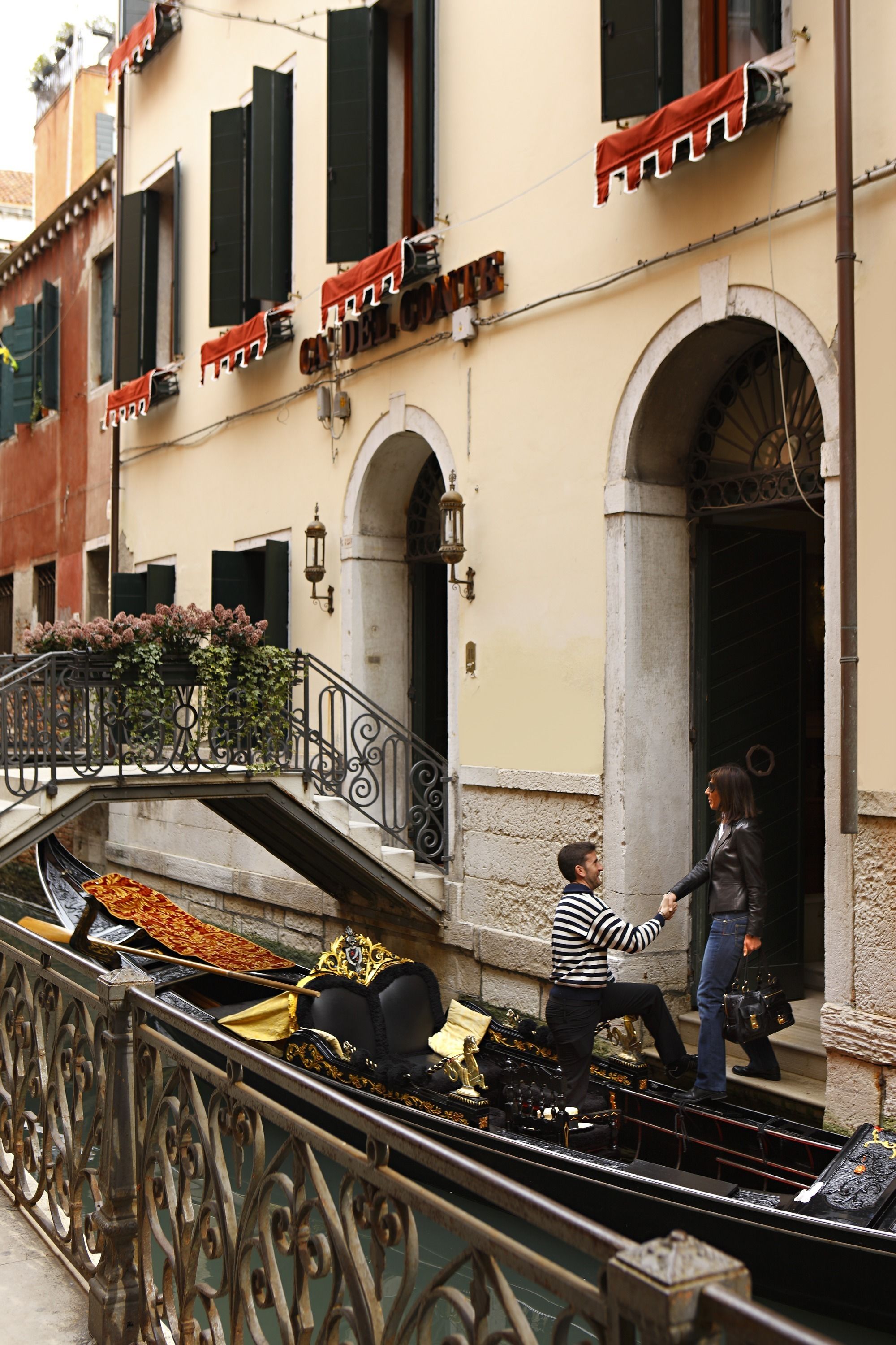 A canal with a gondola, a bridge, and buildings with balconies and shutters.