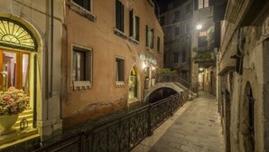 A narrow street with buildings on either side, a small bridge, and a well-lit entrance with a flower arrangement. - Ca' Dei Conti (Venice)