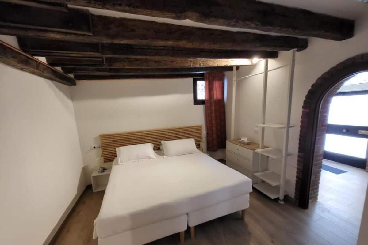 Un dormitorio con una cama grande, vigas de madera, una mesita de noche y un armario.