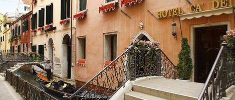 A hotel with a sign reading "HOTEL CA' DEI" and a canal in front.