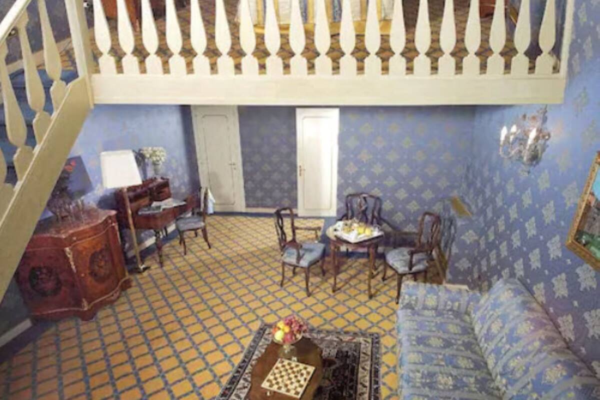 Una habitación con techo alto, balcón con barandilla, piso estampado y candelabro.