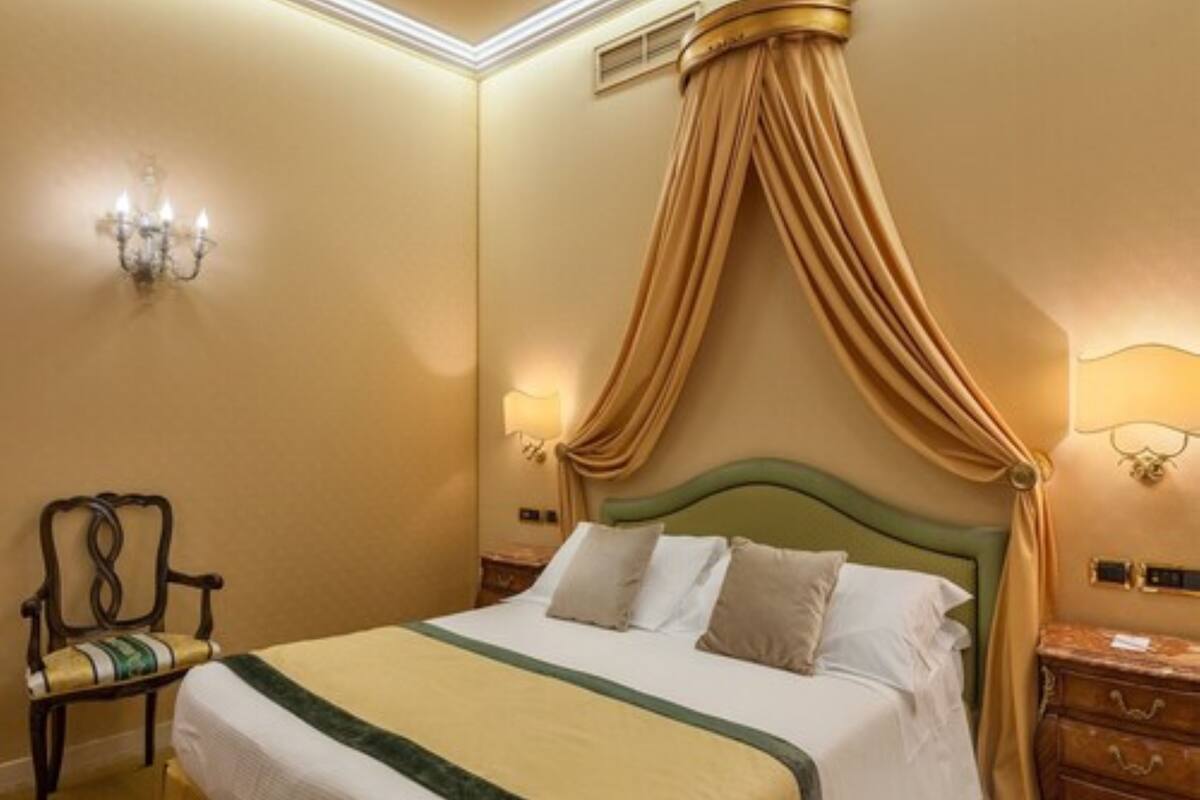 Una habitación de hotel con una cama, una silla, una mesita de noche y una lámpara de pared.