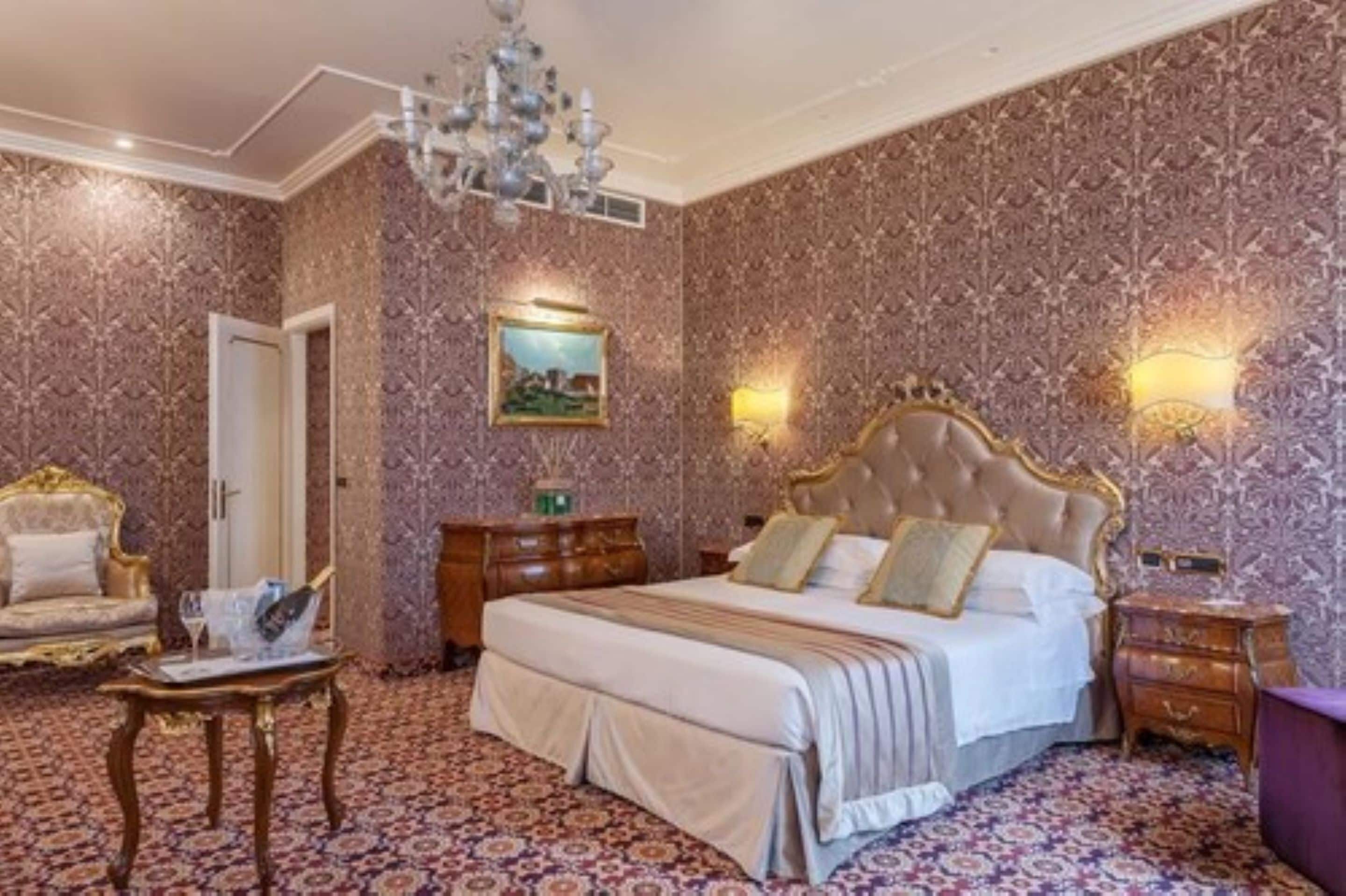 A luxurious bedroom with a large bed, ornate headboard, and patterned wallpaper.