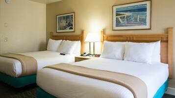 Two double beds with beige and teal bedding, a nightstand with a lamp, and two framed pictures on the wall.