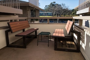 Un balcone con una panca di legno, un tavolino e uno sgabello in metallo.