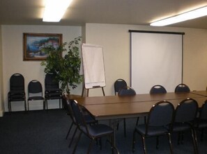 Une salle de conférence avec une longue table, six chaises, un écran de projection, un tableau blanc et un tableau accroché au mur.