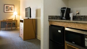 Una kitchenette compacta equipada con refrigerador, microondas, cafetera y un pequeño comedor con una silla y mesa.