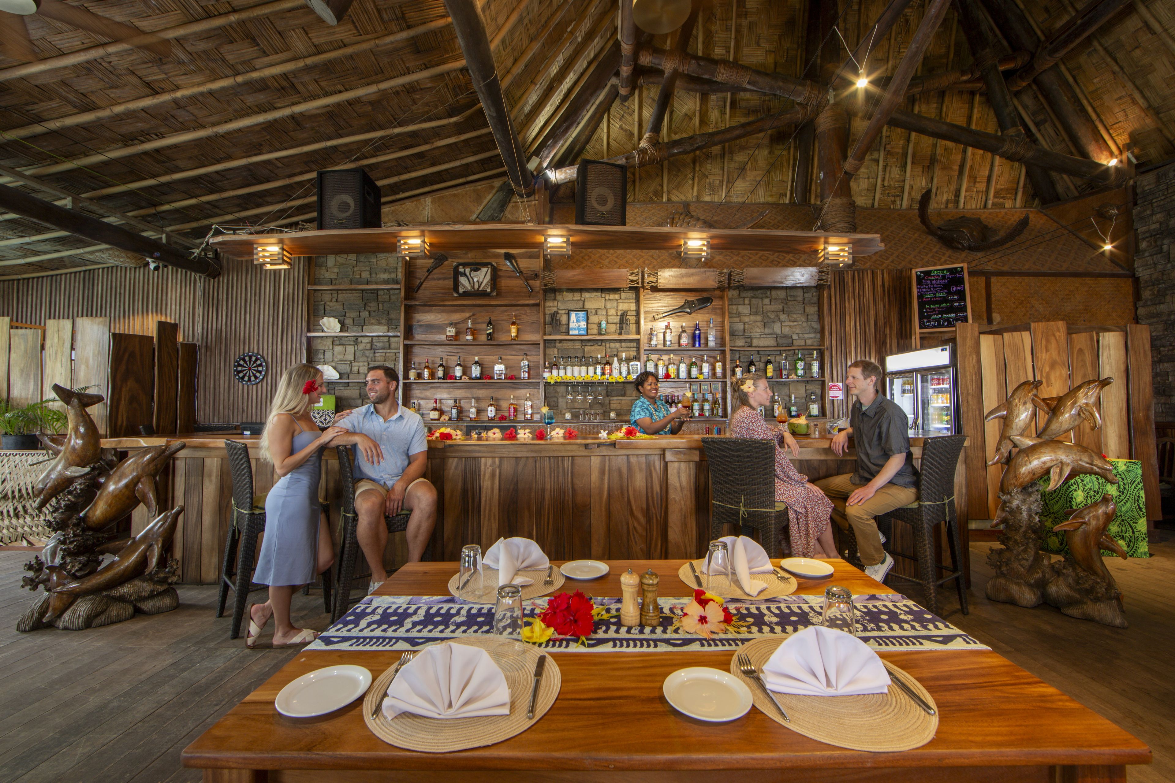 Una zona de bar rústica con vigas de madera, barra y estanterías con botellas.